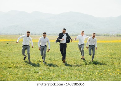Groomsmen and groom running outdoors on the wedding day. Funny wedding moment for best groom friends. Mens hug each other. 
