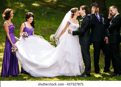 Groomsmen Look Funny Standing Behind A Kissing Wedding Couple