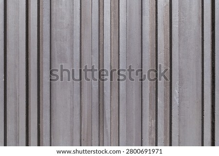 Grooved concrete wall texture with vertical lines. Modern minimalist architectural background featuring a dark grey ribbed stone surface with stripes.