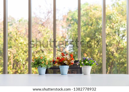 Grop of bouquet colorful artificial flower in vase on modern table with nature outside long glass windows in sunshine day.