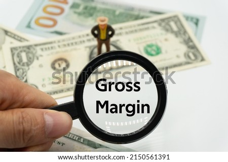 Gross Margin.Magnifying glass showing the words.Background of banknotes and coins.basic concepts of finance.Business theme.Financial terms.