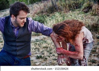 A grotesque and bloody female zombie bites a man's arm