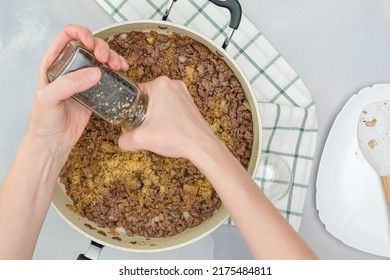 Ground beef, chopped onion, and garlic seasoning close up on frying pan. Chef adds black pepper. Close up cooking process, view from above