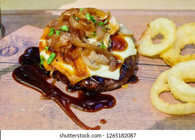 Ground Beef Steak On A Wooden Tray N Soft Focus.With Sauce Topped. With Cheese And Onions Placed On Top Of The Steak And Fried Onion Beside. At The Restaurant