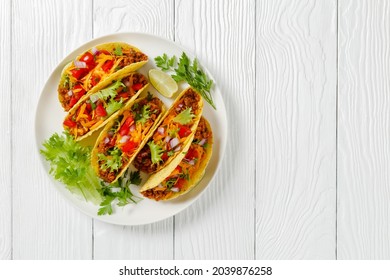 Ground Beef Tacos with shredded cheddar cheese, fresh lettuce, tomato, onion on a white plate with lime wedges, horizontal view from above, mexican cuisine, flat lay, free space - Powered by Shutterstock