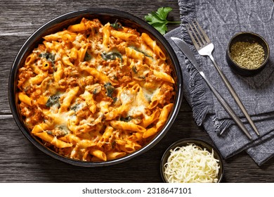 Ground Chicken Pasta Bake with onion, mushrooms, spinach, tomato sauce and mozzarella cheese in baking dish on dark wood table