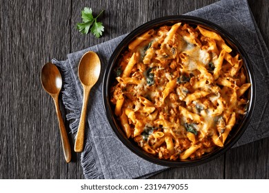 Ground Chicken Pasta Bake with onion, mushrooms, spinach, tomato sauce and mozzarella cheese in baking dish on dark wood table with spoons, horizontal view from above, flat lay, free space