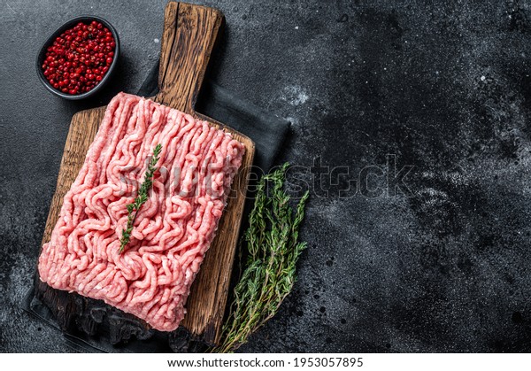 Ground chicken or turkey raw meat on\
wooden board. Black background. Top View. Copy\
space