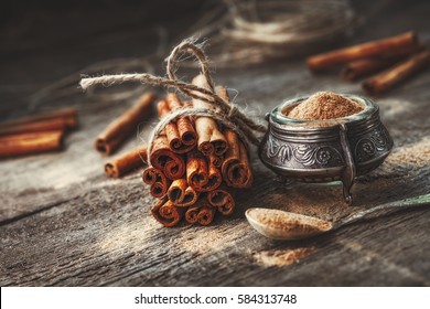 Ground cinnamon, cinnamon sticks, tied with jute rope on old wooden background in rustic style