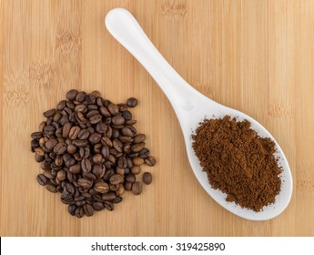 Ground Coffee In Plastic Spoon And Heap Of Coffee Beans On Wooden Table