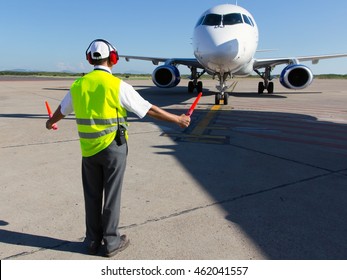 Ground Crew in the signal vest. Aviation Marshall / Supervisor meets passenger airplane at the airport. Aircraft is taxiing to the parking place.