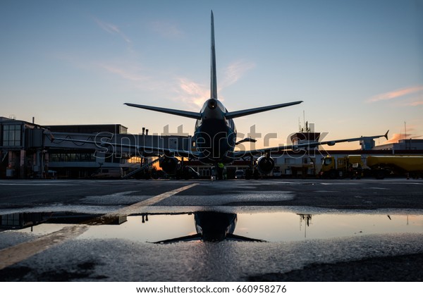 Ground handling of a passenger\
airplane parked to a jet bridge with reflection in a\
puddle