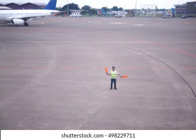 Ground handling personal giving an aircraft marshalling signal at the airport. Blurred background.