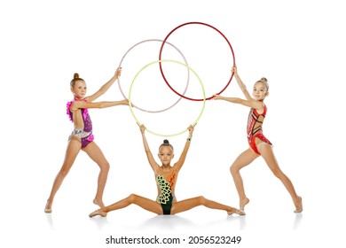 Ground hoop routine. Young and flexible. Beautiful rhythmic gymnastics artists, girls posing isolated on white studio background. Concept of sport, team, achievements, education, active lifestyle - Powered by Shutterstock