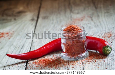 Ground hot red pepper in a glass jar and fresh chili peppers on old wooden background, selective focus