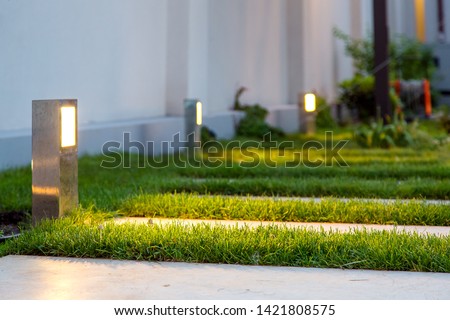 ground lantern lighting marble walkway in the evening park with a green lawn, closeup lantern illumination warm light marble pavement.