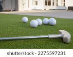 A ground level closeup view of several golf balls and putter, in a backyard putting green setting.