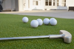 A Ground Level Closeup View Of Several Golf Balls And Putter, In A Backyard Putting Green Setting.