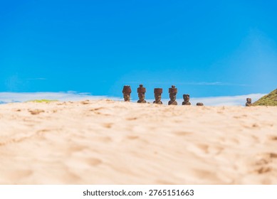 Ground level shot of Ahu Nau Nau Moai statues with red pukao hats. Blurred white sand foreground and clear blue sky on Easter Island, Chile. Minimalist travel photography