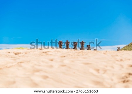 Ground level shot of Ahu Nau Nau Moai statues with red pukao hats. Blurred white sand foreground and clear blue sky on Easter Island, Chile. Minimalist travel photography