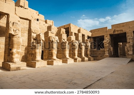 Ground level view of a row of ancient pharaoh statues standing against hieroglyph-covered sandstone walls inside the Karnak Temple complex in Luxor, Egypt. 