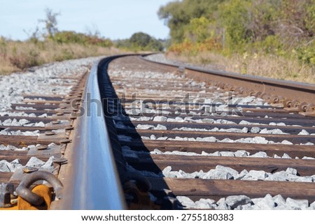 Ground level view of train tacks curving into the distance, with wooden sleepers and rails in sharp focus.  Dried grasses and the surrounding vegetation create a natural and rustic outdoor scene.