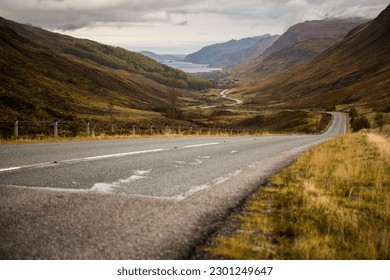 Ground level view of a winding road across a valley leading to a lake surrounded by misty mountains in the Scottish Highlands, United Kingdom - Powered by Shutterstock