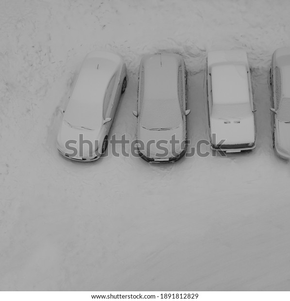 Ground parking cars after snowfall,\
view from above. Automobiles covered with snow. top view. Free\
space is on the winter parking lot in the line of snowy\
cars