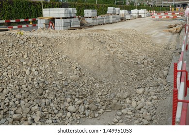 Ground Prepared For A Civil Engineering Building Site With Cement Stones Or Tiles And Other Building Material In The Background Together With Red And White Barrier Planks Ans A Sign Work On Road Ahead