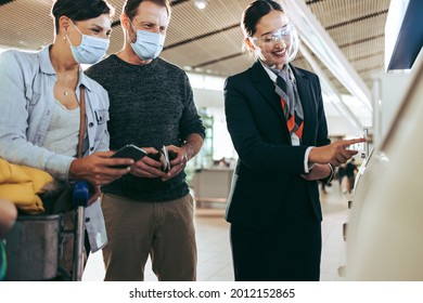 Ground Staff Helping Couple With Self Service Check-in During Pandemic. Man And Woman In Face Masks Helped By Airlines Attendant At Airport In Pandemic.