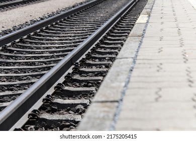 Ground view of railroad tracks running diagonally through the image with partially visible platform as a concept for train travel stations and railroad traffic