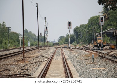 Ground-level view of intersecting railway tracks with red signal lights in a countryside setting. Infrastructure, transportation network, and industrial rail system concept.