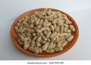 Groundnut, Goober or Monkey Nut, or Arachis hypogaea, on a wooden plate, isolated in white background. Ready to eat as snack