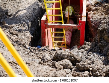Groundworker Installing Clay Drainage Pipe While In The Trench Supported By Trench Box