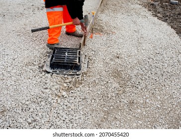 Groundworker In Orange Safety Hi Vis Trousers Fixing A Timber Along String Line With Steel Pin To Form A Kerb Riser And A Straight Edge For Tarmac Road Surface During New Road Construction