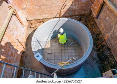 Groundworker working in new built deep manhole during drainage works marking for pipes position