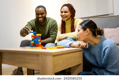 A group of 3 multiethnic friends play board games in a cozy apartment.The African man is placing a piece on the wooden tower.Concept of friends playing at home.Zero technology. - Powered by Shutterstock