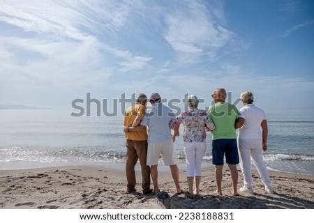 group of 5 seniors at the beach standing together looking at the horizon in the distance
