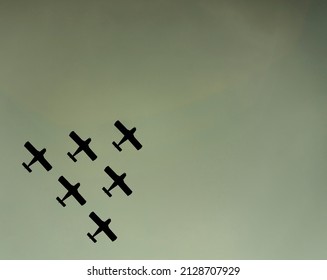 Group of 6 military planes in triangle formation, flying overhead in the sky. Camera angle looking up. Clear sky. Plane is a black silhouette shape. Concept for war. Planes on the bottom right.