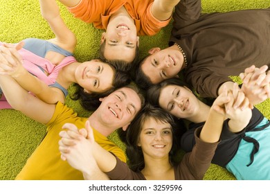 Group of 6 teenagers lying on the floor head next to head. They're looking at camera and smiling. They're holding their hands up. - Shutterstock ID 3259596