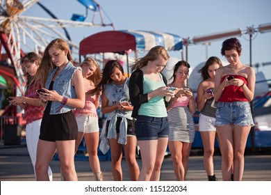 Group of 8 teenage girls text messaging at an amusement park
