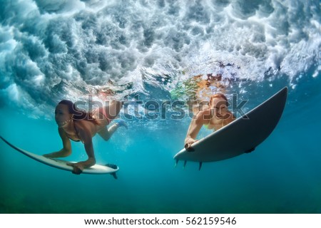 Group of active girls in action. Surfer women with surf board dive underwater under breaking big wave. Healthy lifestyle. Water sport, extreme surfing in adventure camp on family summer beach vacation