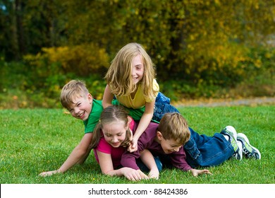 A Group Of Active Kids Playing In A Dog Pile On Grass.