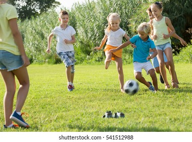 Group of active kids in school age happily playing football together on green lawn in park