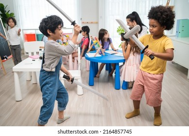 Group of Active mixed race young little kid playing sword in schoolroom. Student child girls and boys spending time play rapier toy  while during break with feeling fun together in classroom at school