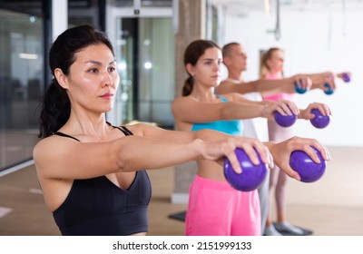 Group of active people engaged in fitness in the studio perform various exercises, holding special small Pilates balls in ..their hands