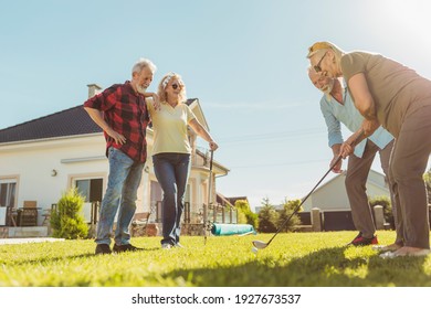 Group Of Active Senior Friends Having Fun Playing Mini Golf At The Backyard Lawn, Spending Sunny Summer Day Outdoors