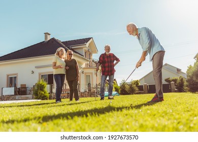 Group Of Active Senior Friends Having Fun Playing Mini Golf At The Backyard Lawn, Spending Sunny Summer Day Outdoors