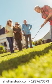 Group Of Active Senior Friends Having Fun Playing Mini Golf At The Backyard Lawn, Spending Sunny Summer Day Outdoors