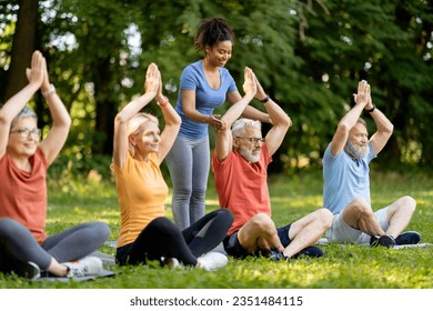 Group of active senior people in sportrswear attending outdoor yoga class with instructor, mature friends meditating with hands above head, sitting on fitness mats, enjoying healthy lifestyle - Powered by Shutterstock